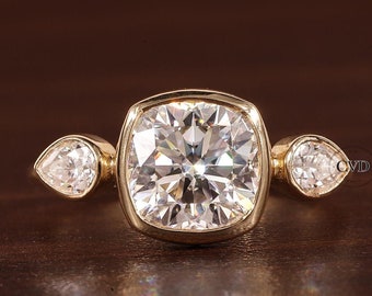 Puede incluir: Un anillo de oro con un gran diamante de forma cuadrada en el centro y dos diamantes más pequeños en forma de pera a cada lado.