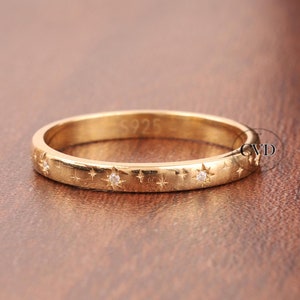 May include: A gold band ring with a delicate star design and small clear stones. The ring is engraved with the number "925".