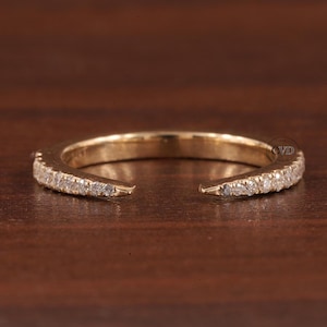Op de afbeelding: Een gouden ring met een rij kleine diamanten die in de band zijn gezet. De ring is aan één kant open, waardoor het een halve eeuwigheidsband is.