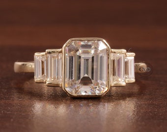 Puede incluir: Un anillo de oro con una gran piedra central de corte esmeralda y piedras más pequeñas de corte baguette a cada lado.
