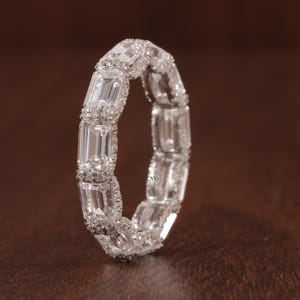 Può includere: Un anello a fascia d'argento con una fila di diamanti a taglio smeraldo incastonati a pavé.