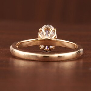 May include: A gold engagement ring with a round, clear gemstone. The ring has a delicate, floral-inspired setting that holds the central stone. The band is smooth and polished, reflecting the light.