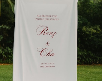 Pode incluir: Uma faixa de tecido branco com texto bordô. A faixa diz "ALL BECAUSE TWO PEOPLE FELL IN LOVE" acima dos nomes "Renz & Cha" e a data "29.09.2025" com "THE LANGHAM" abaixo. A faixa está pendurada ao ar livre.