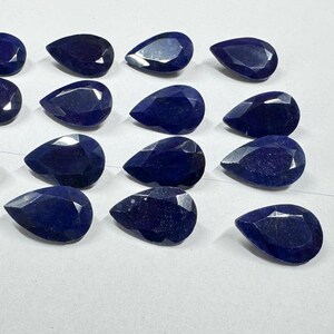 May include: A selection of deep blue, pear-cut gemstones. The gems are arranged closely together, displaying their polished surfaces and the way light catches their facets. The overall effect is one of luxury and elegance. Each gem is approximately 1-2 cm in length.