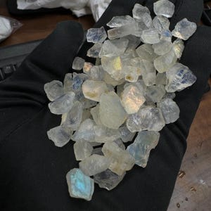 May include: A collection of iridescent white moonstone chips. The chips are various sizes and shapes, with some showing a rainbow sheen.