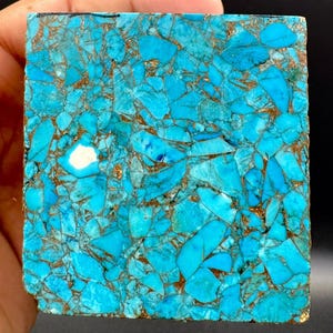 May include: A square slab of composite turquoise stone featuring a vibrant mosaic of bright blue fragments held together by a dark brown matrix. The surface displays a dense, irregular pattern of angular turquoise pieces with one small white spot.