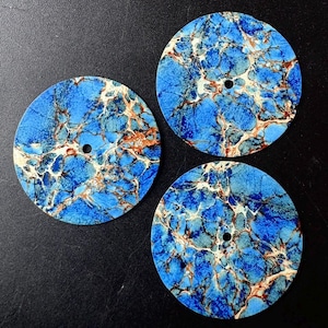 Può includere: Tre dischi piatti circolari caratterizzati da un vivace motivo blu simile al marmo, con intricate venature bianche e color rame. Ogni disco presenta un piccolo foro circolare centrale, creando un aspetto uniforme per tutti e tre i pezzi.