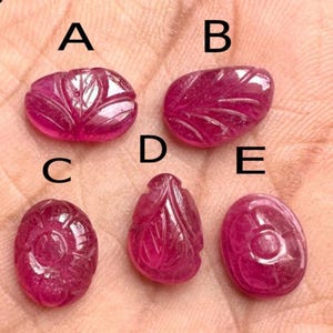Op de afbeelding: Vijf gesneden robijn edelstenen in verschillende vormen. De edelstenen hebben een dieproze kleur en hebben ingewikkelde blad- en bloemontwerpen. De edelstenen zijn gelabeld met A, B, C, D en E.