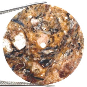 May include: A circular watch dial featuring a mottled, multi-colored stone pattern with shades of brown, tan, black, and white. The surface has a natural, textured appearance with a central hole and a small hole near the bottom edge for markers.