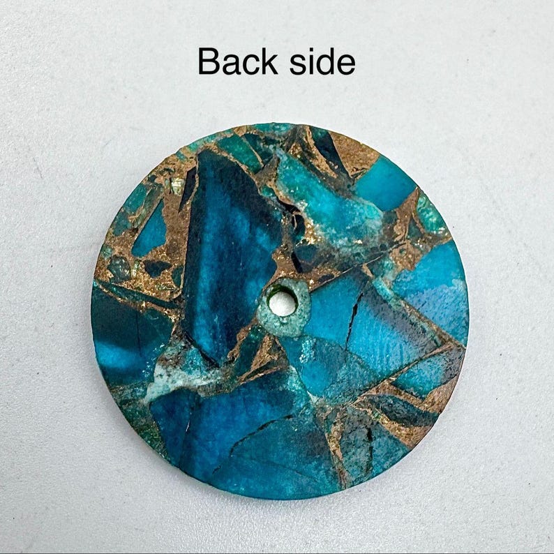 May include: A round, teal and gold-colored stone pendant with a hole drilled through it. The stone has a mosaic-like pattern with a mix of teal and gold colors. The text "Back side" is visible at the top.