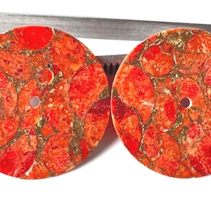 May include: Two circular, flat, red and orange patterned stone beads with a central hole. The surface features a mosaic-like appearance with vibrant red, orange, and gold-toned inclusions throughout the material, creating a textured look.