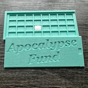 May include: A light teal 3D-printed tray with a grid of small squares and the words "Apocalypse Fund" embossed on the bottom half. A small, silver square is in one of the grid spaces.