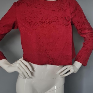May include: A red long-sleeved crop top with a damask pattern.