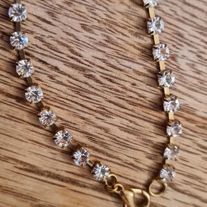 May include: A gold chain bracelet with clear rhinestones. The bracelet has a lobster clasp closure.