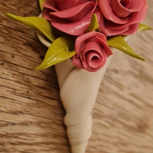 May include: A bouquet of three pink roses with green leaves in a white ceramic cone-shaped vase.