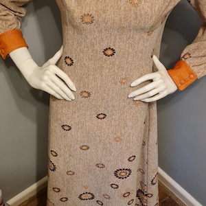 May include: A long-sleeved dress with a brown and orange floral pattern. The dress has a high neck and a fitted bodice. The sleeves are long and have orange cuffs. The dress is made of a soft, textured fabric.