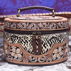May include: A brown leather round box with a tooled floral design and a black and white animal print lining. The box has a brown leather handle and a zipper closure.