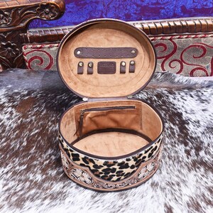May include: Open, oval-shaped jewelry case with a brown leather exterior and a leopard print band. The interior is lined with tan fabric and features storage compartments for jewelry. The case is open, revealing its contents.