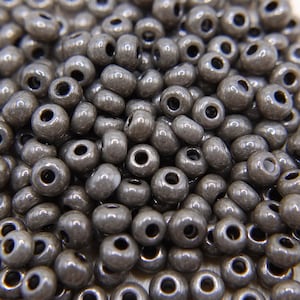 Könnte beinhalten: Nahaufnahme eines Haufens metallisch grauer Perlen. Die Perlen sind klein, zylindrisch und haben ein Loch in der Mitte. Die Oberfläche der Perlen hat ein leicht strukturiertes Aussehen und sie sind zufällig verstreut.