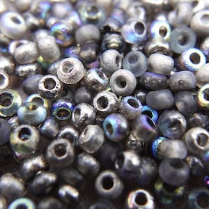 Könnte beinhalten: Nahaufnahme einer Auswahl kleiner, runder Glasperlen in Grautönen, Silber und irisierendem Blau. Die Perlen haben eine strukturierte Oberfläche und sind perfekt für die Schmuckherstellung.