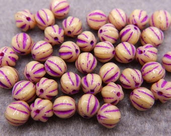 Könnte beinhalten: Eine Sammlung cremefarbener Perlen mit violetten Streifen. Die Perlen sind rund und haben eine strukturierte Oberfläche.