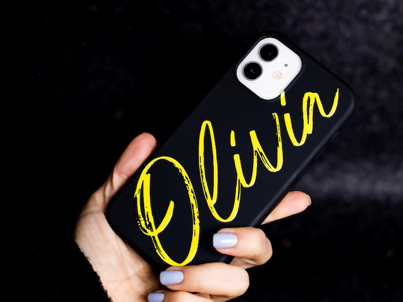 May include: Black phone case with a yellow "Olivia" name written in a brushstroke font.