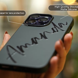 May include: A gray phone case with a raised bezel for lens protection. The case has a matte finish and the name "Amanda" is written in black across the back.