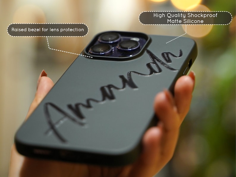 May include: A gray phone case with a raised bezel for lens protection. The case has a matte finish and the name "Amanda" is written in black across the back.