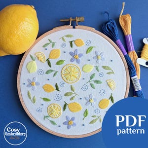 Puede incluir: Un patrón de bordado PDF para un diseño de limón y flores. El patrón se muestra en un aro de bordado de madera con tela blanca e hilo de bordar de colores.
