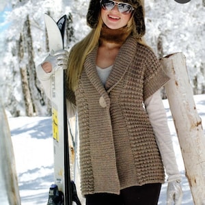 May include: A brown knitted cardigan with a button fastening and short sleeves. The cardigan is worn over a white shirt and black trousers. The person is wearing a brown fur hat with a white brim and sunglasses. The person is holding a pair of skis.