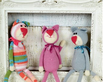 May include: Three handmade crochet cat dolls in a white framed display. The dolls are in pink, blue, and striped patterns. Each cat has a red nose and a bow. The image includes text that says "4 Crochet designs".