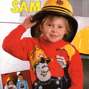 Może przedstawiać: Dziecko w czerwonym swetrze z postacią strażaka z kreskówki, żółtym hełmem i napisem "Fireman Sam". Obraz zawiera również tekst "Wash'n'Wear Double Crepe".
