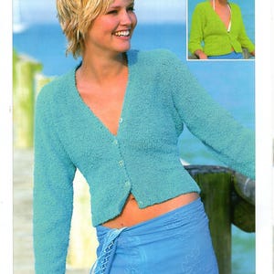 May include: A light blue cardigan with a v-neck and button closure. The cardigan is made of a soft, textured yarn. The model is wearing the cardigan with a blue skirt.