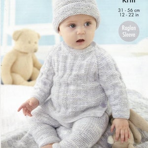 May include: A baby wearing a gray knitted sweater and pants set with a matching gray knitted hat with a white pom pom. The set is labeled "double knit" and "raglan sleeve". The baby is sitting on a white blanket with a teddy bear and a bunny toy.