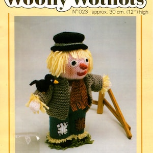 May include: A knitted scarecrow doll with a black hat, brown jacket, blue jeans, and a black bird perched on its shoulder. The doll is 12 inches tall and is part of a knitting pattern collection called "Woolly Wotnots".