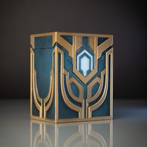 Peut inclure: Une boîte décorative bleu-vert et dorée avec des motifs géométriques. La boîte est carrée avec des accents dorés et un emblème blanc central et lumineux. Le design est symétrique et présente des lignes et des formes stylisées.