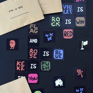 May include: A collection of colorful stickers with pixelated designs and text. The stickers feature phrases like "Baba is Rose", "Violet is Red", and "Rock is Win".