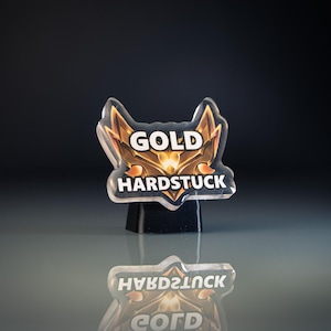 May include: A clear acrylic emblem with the words "GOLD HARDSTUCK" in white lettering. The emblem has a gold and brown design. The emblem is standing on a black base, with its reflection visible below.