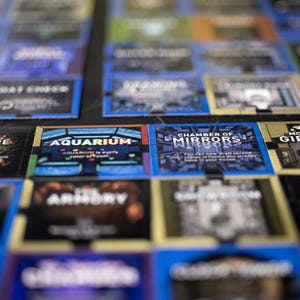 Puede incluir: Una colección de fichas cuadradas de juego de mesa con varios nombres de habitaciones e ilustraciones. El texto visible incluye Aquarium, Chamber of Mirrors, The Armory y Mountain Gift. Las fichas están dispuestas en una cuadrícula con bordes azules, dorados y negros.