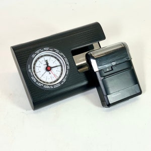 Puede incluir: Un reloj de viaje negro con un dial de zona horaria mundial y una afeitadora eléctrica negra con la palabra "Panasonic" en ella.