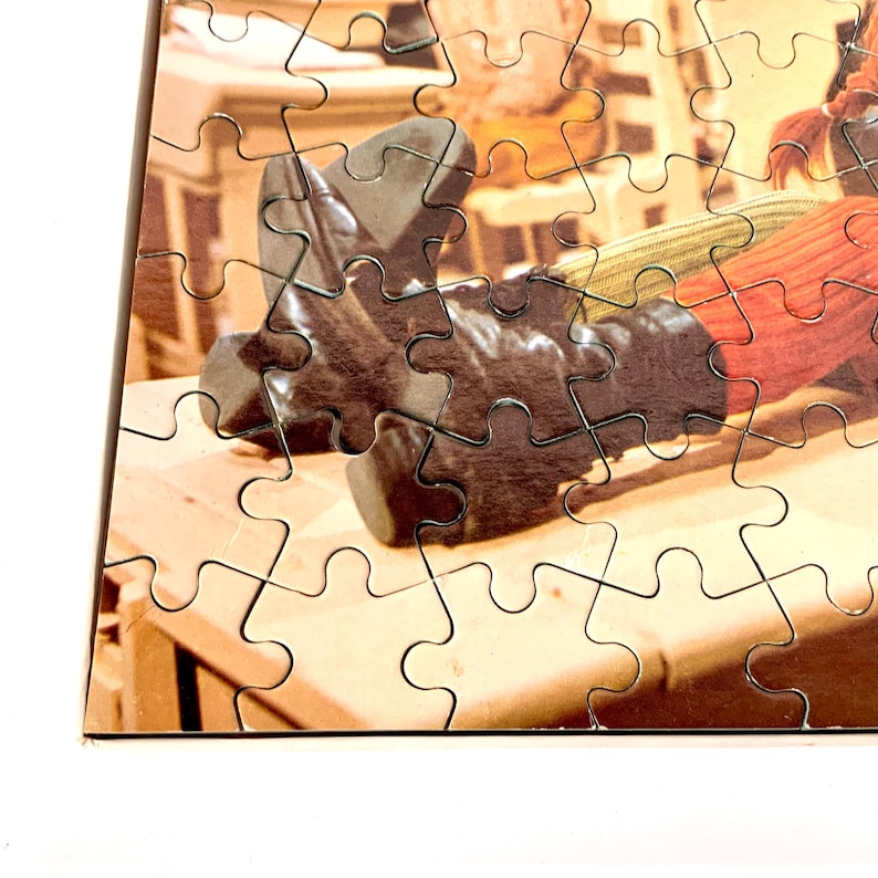 May include: A partially assembled jigsaw puzzle featuring a photograph of a pair of black leather boots. The boots are resting on a wooden surface, with other items in the background. The puzzle pieces are interlocking, with a white border.