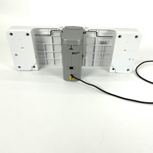 May include: A white and gray electronic device with a black power cord. The device has two white, rectangular sections on either side of a gray, central component. The central component has a yellow port.