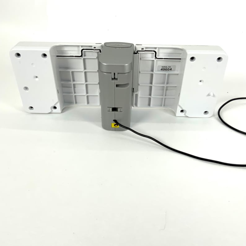 May include: A white and gray electronic device with a black power cord. The device has two white, rectangular sections on either side of a gray, central component. The central component has a yellow port.