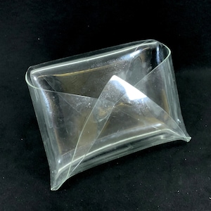 Puede incluir: Un plato de plástico transparente con forma de sobre y diseño plegado. El plato está hecho de un material translúcido y tiene un acabado liso y brillante.