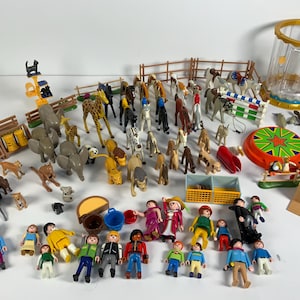 Puede incluir: Una colección de juguetes de plástico de colores: animales, figuras y accesorios de granja. Incluye jirafas, elefantes, caballos, cebras y personas. Hay un tiovivo, una valla y una jaula. Los juguetes están colocados sobre una superficie blanca.