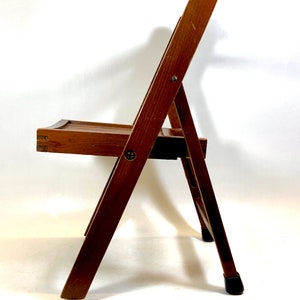 May include: A brown wooden folding chair with a simple design. The chair has a seat and back made of wood slats. The chair is in a folded position, with the back resting on the seat. The chair has a metal hinge and a metal footrest.