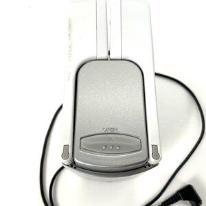 May include: A white and silver electronic device with a black cord. The device has a silver center with the word "OPEN" and three small dots. The top and sides are white. The cord has a right-angle connector.