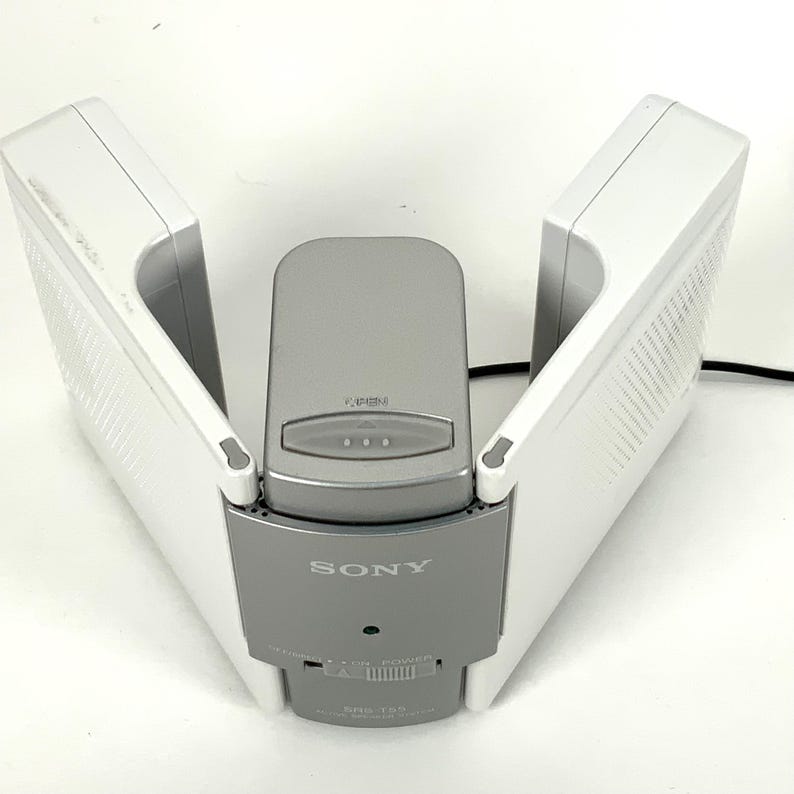 May include: A white and gray Sony battery charger. The charger has two white wings that open and close, with a gray center section. The Sony logo is visible on the front. The model number is visible on the front.