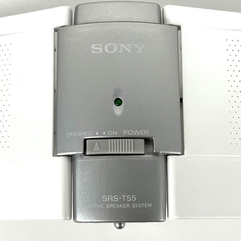 May include: A silver and white Sony SRS-T55 five speaker system. The speaker system has a power button and a green light. The Sony logo is visible on the front. The speaker system is white on the sides.