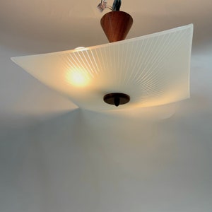 May include: A white ceiling light fixture with a wood and metal base. The light fixture has a white frosted glass shade with a sunburst pattern.